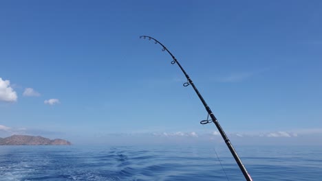 Eine-Solo-Angelrute,-Die-An-Einem-Perfekten-Tag-Mit-Schönem-Wetter-Und-Ruhigen-Seebedingungen-Auf-Einem-Fahrenden-Boot-Vor-Einem-Blauen-Himmel-Und-Einer-Meereskulisse-Trollt