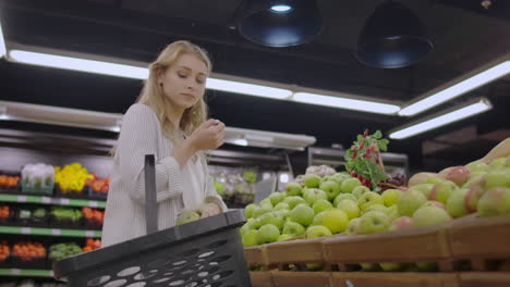 joven atractiva eligiendo una manzana en el mercado de frutas y verduras del supermercado