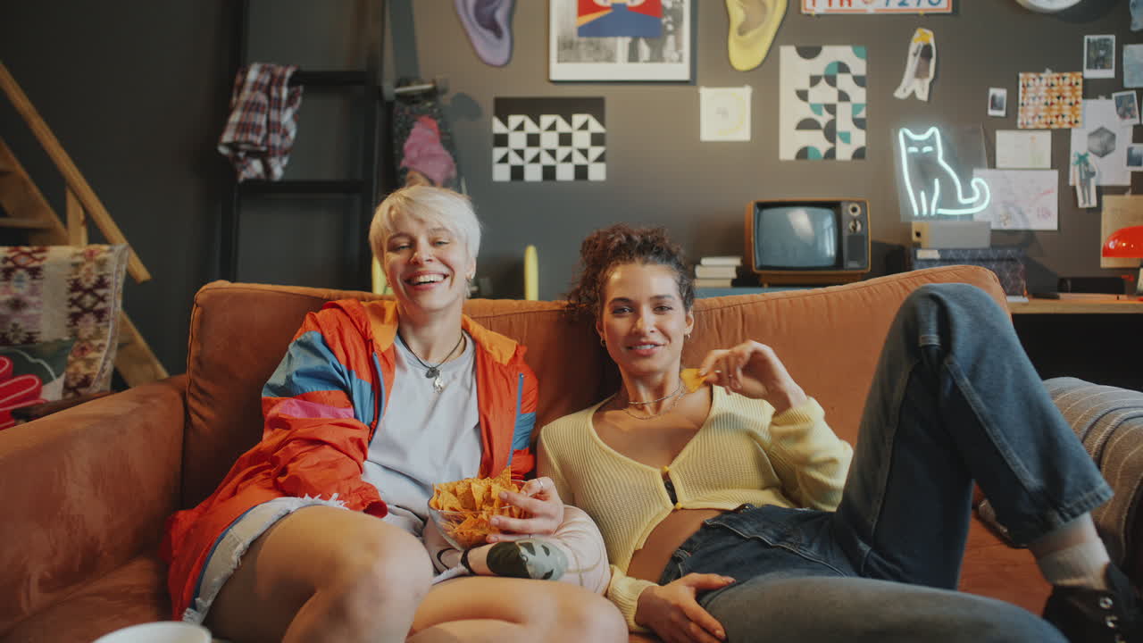 Happy Female Friends Eating Chips and Laughing at Comedy Show on TV