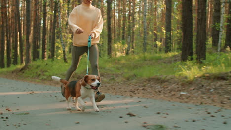 woman running with her beagle dog in a forest