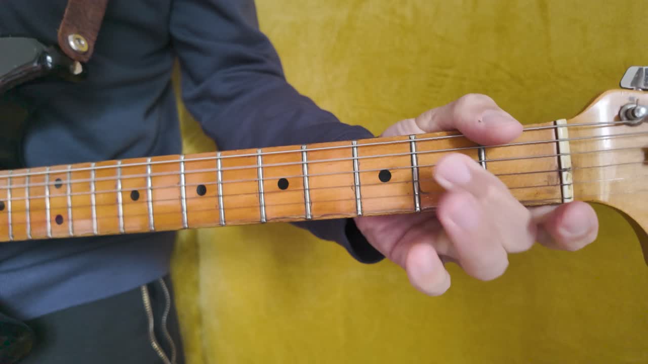 Close up of hand playing a vintage electric guitar against a yellow background