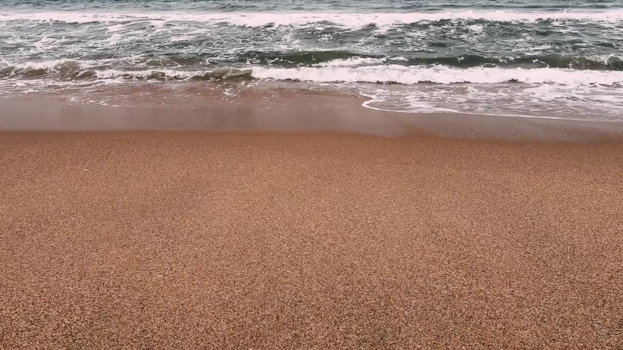 Niedrige POV-Aufnahme einer Strandwelle, die auf die Kamera zukommt. Statisch.
