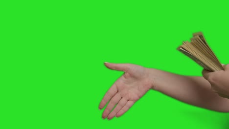 a male hand holds out a large bundle of money to a female hand, making a transaction, green screen