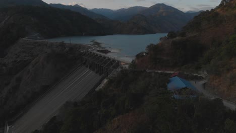 Ambuklao-hydroelectric-Dam-revealing-the-water-reserve-lake-behind-it-surrounded-by-trees-and-mountains-in-remote-area-Luzon,-Bokod,-Benguet,-Philippines-Left-Panning-Aerial