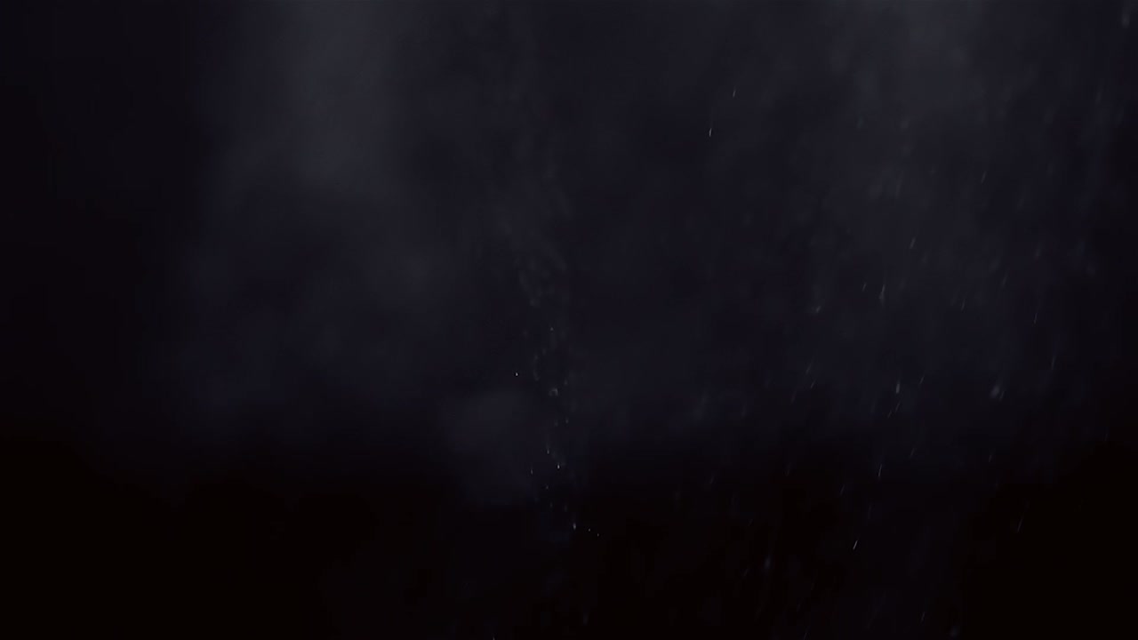 Misty spray water droplets shimmer in soft light as they fade against black background