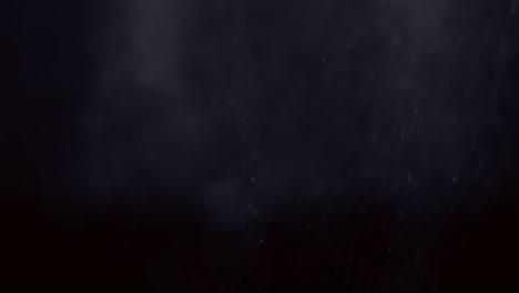 misty spray water droplets shimmer in soft light as they fade against black background