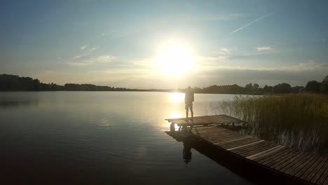 A-silhouette-shot-of-a-teenager-who-is-standing-at-the-bridge-with-his-arms-on-his-head-looking-at-the-sun-while-the-golden-hour