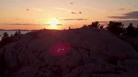 inukshuk on rocky pine tree island at sunset, drone aerial wide pedestal up