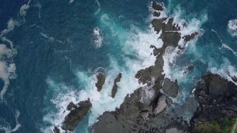 overhead shot of big waves of indian ocean hitting boulder and rocks in the beach in sunny condition weather - pengilon hill, indonesia, asia