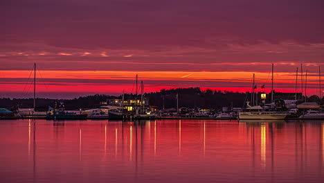 timelapse of a red sunrise in a dock full of moored boats, with reflections of calm water