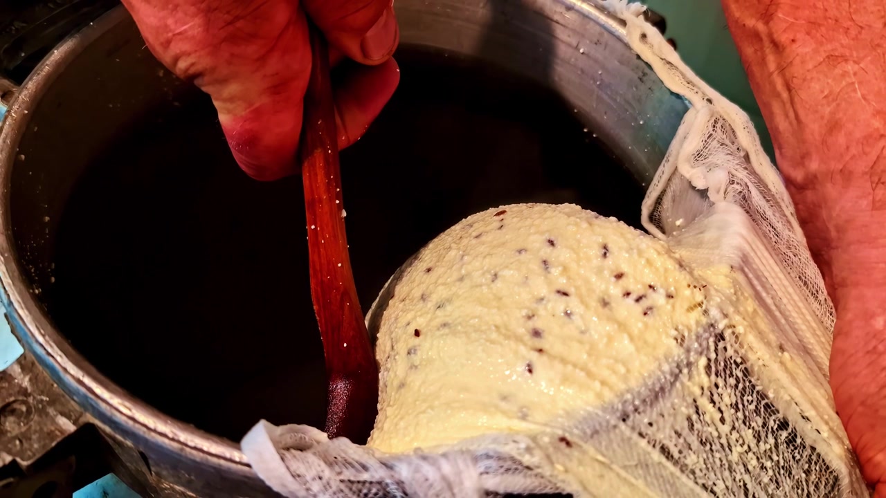 Close-up of a cheesemaker stirring a pot while draining homemade flaxseed cheese in cheesecloth