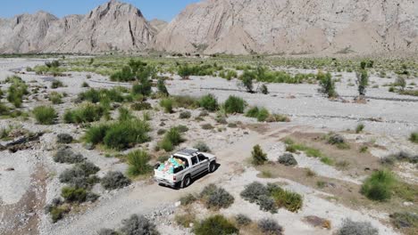 Aerial-shot-of-car-driving-on-rocky-road-near-the-mountain-in-the-morning-time