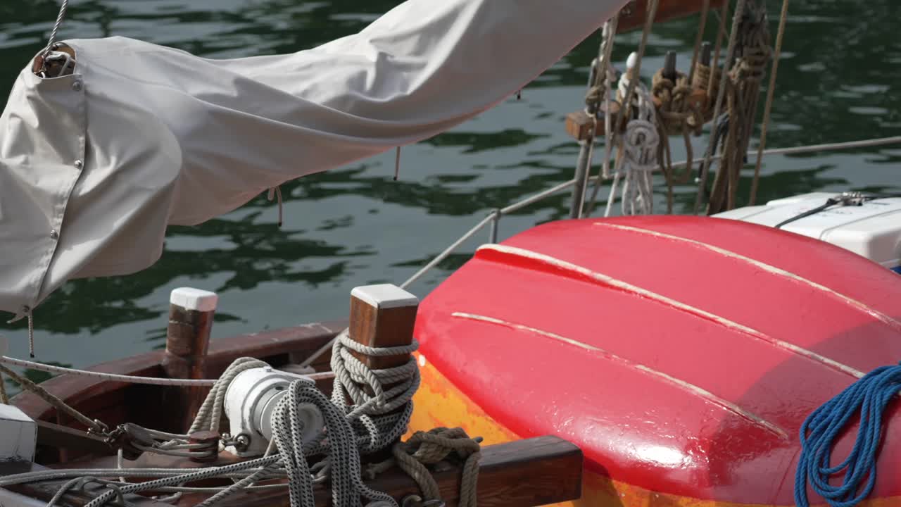 Red kayak resting on sailboat deck, with nautical ropes and wooden details on a calm day