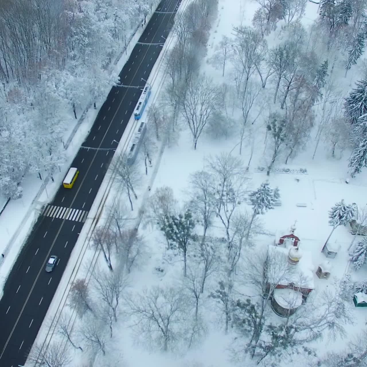 Black two-lane road standing out at the white backdrop of the city landscape. Winter in the city from aerial perspective