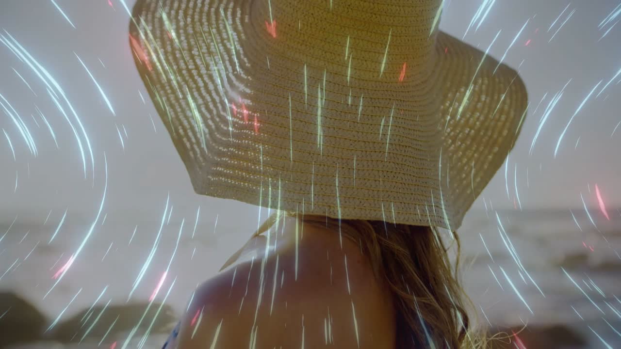 Woman turning back on beach while light streaks starting, sweeping hat and back, promoting travel