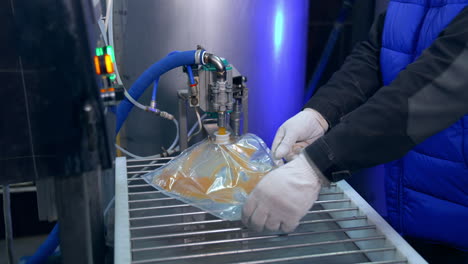 transparent plastic bag being filled with juice through an opening. factory worker smoothes out the bag for better filling of juice.