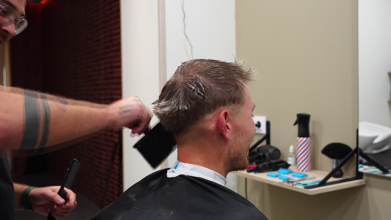 Hairdresser dusts customer’s neck after haircut while he smiles happily