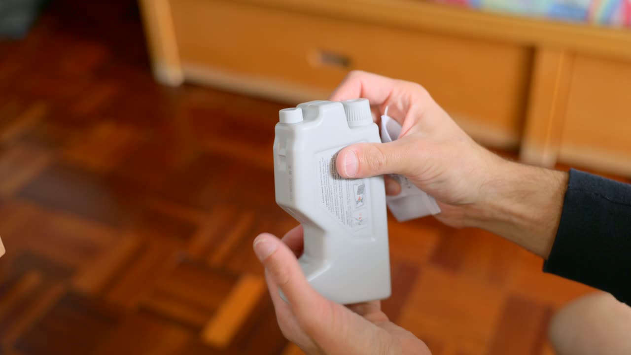 Close-up of a person's hands removing a disposable cleaning pad from the water tank of a robotic mop. Smart home maintenance and cleaning. Ideal for modern technology and home automation concepts