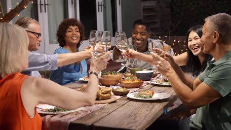 Group-Of-Mature-Friends-Enjoying-Outdoor-Meal-In-Backyard