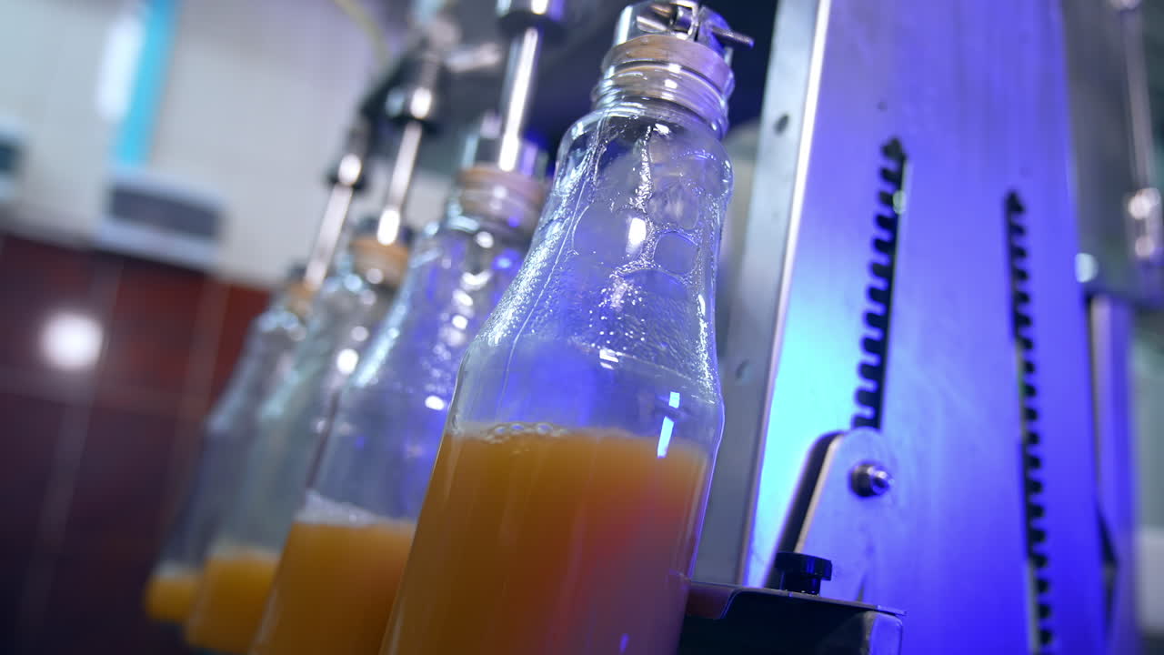 Apple juice being poured into the glass bottles. Close up. Automated line at modern food factory. Blurred background.