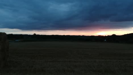 Silhouette-of-agriculture-landscape-and-dark-stormy-clouds-with-bright-sunset-in-horizon,-aerial-view