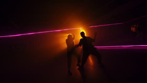 young sportive people perform pair dance in dark studio. contemporary dance style in front of projector.