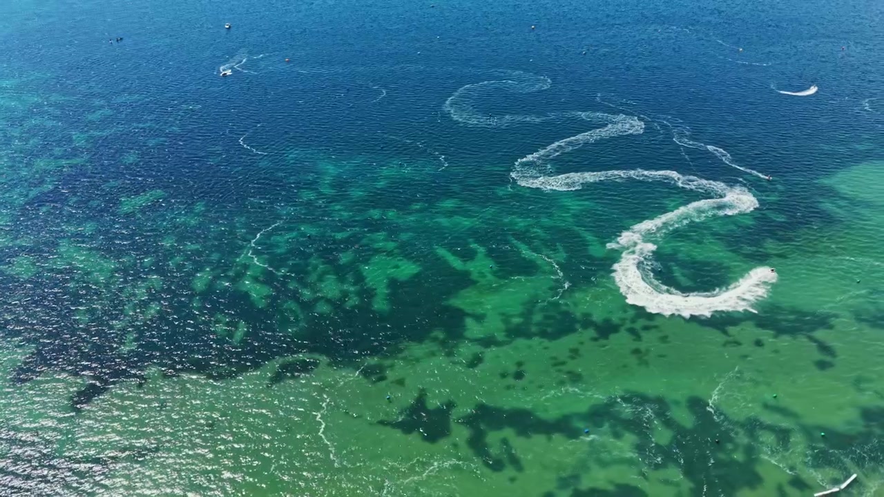 Carreras de motos acuáticas en agua azul cristalina durante el día con estelas visibles dejadas en la superficie
