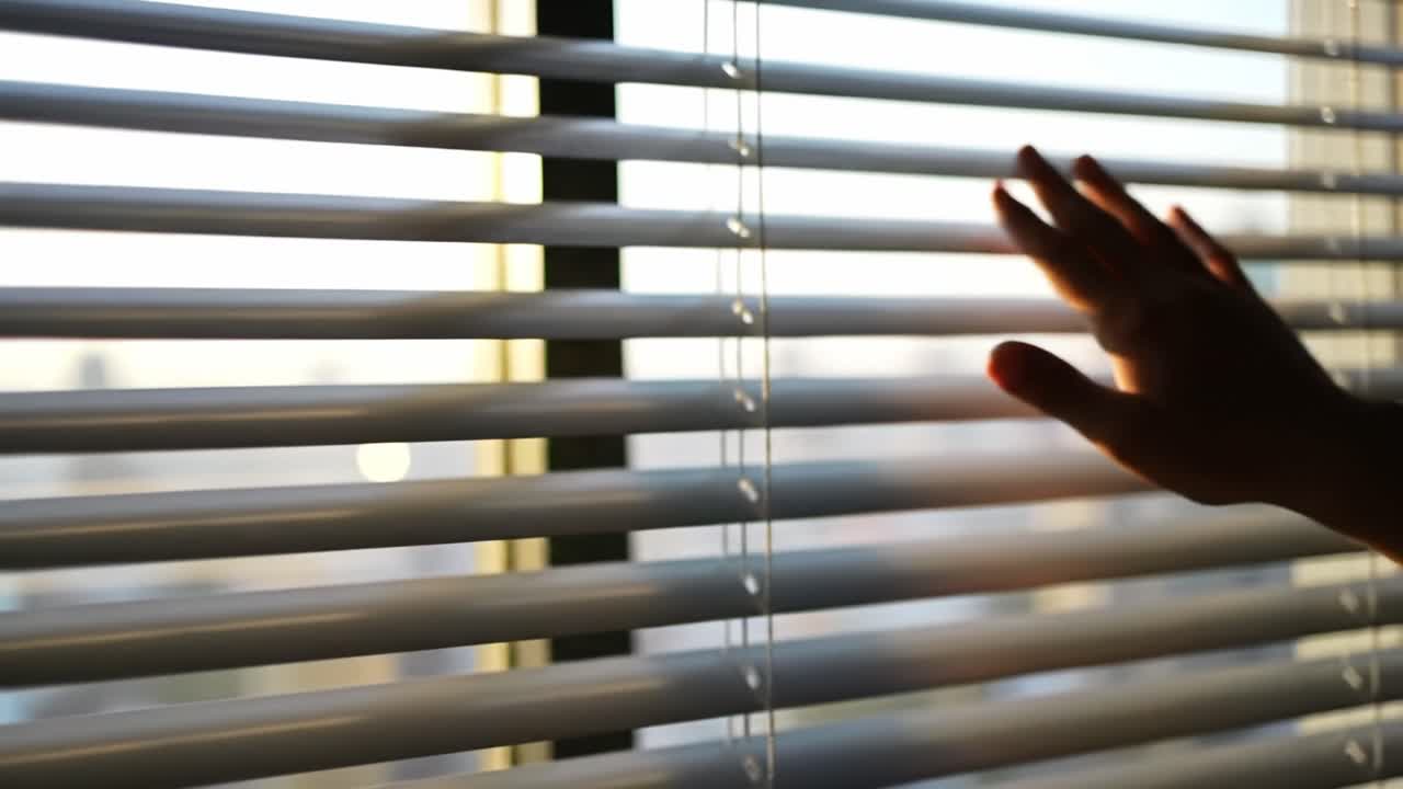 Hand reaching through window blinds