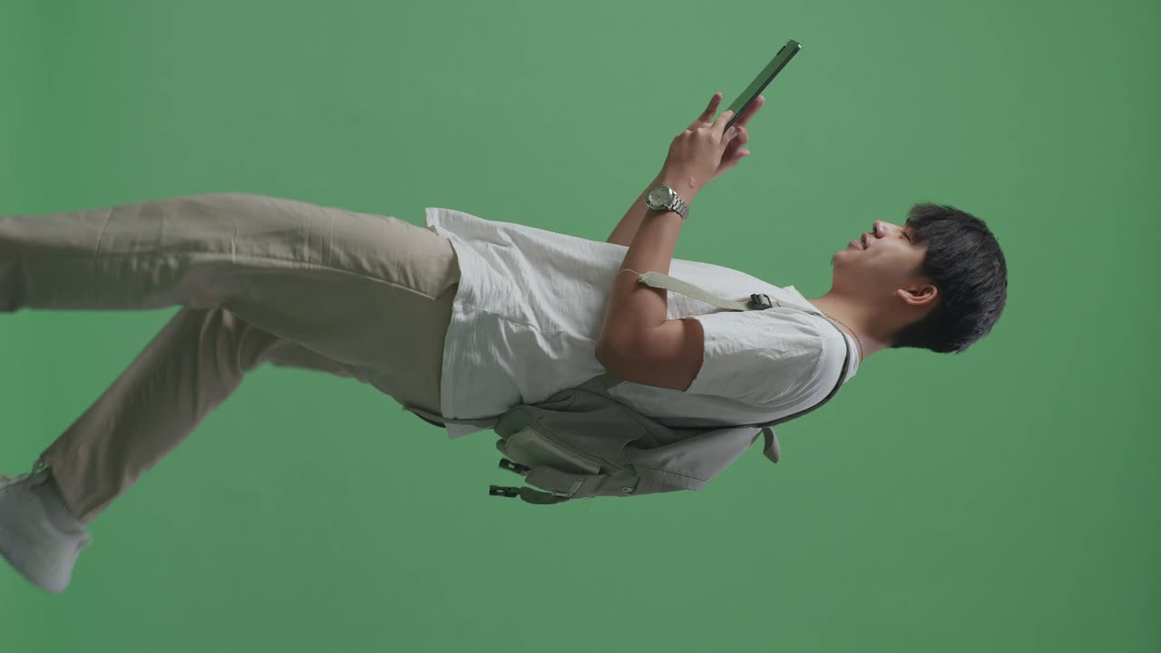 vista lateral de un estudiante asiático usando una tableta y caminando en el estudio de pantalla verde