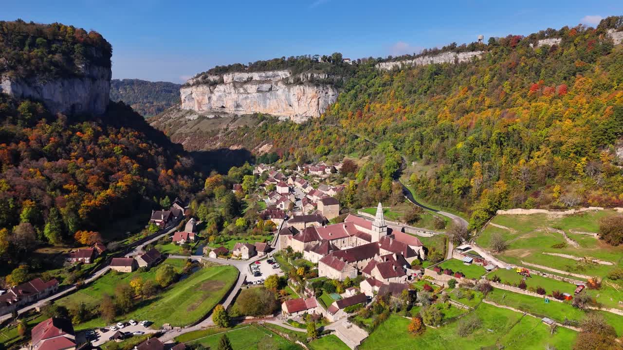 Orbiting drone shot around Baume‑les‑Messieurs village nestled at the end of Reculée de Baume, steep Jurassic limestone cliffs and autumn forests surrounding the valley in the Jura department, France