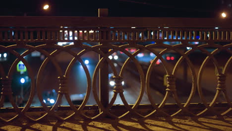 close view of a decorative iron fence with a bokeh effect of city lights and car headlights in the background at night