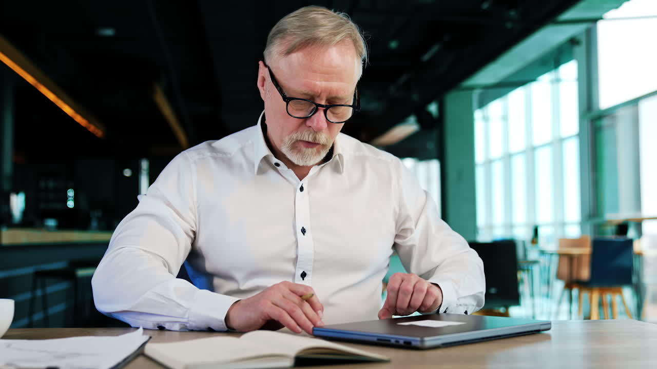 Hard-working man wearing glasses write in his paper book. Businessman decides to use laptop but changes his mind and goes back to writing.