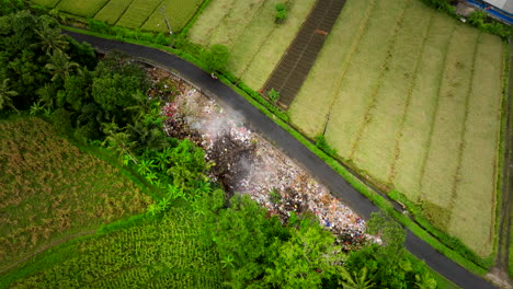 Drone-view-of-smoking-trash-pile-next-to-lush-green-farm-lands-in-Bali-Indonesia