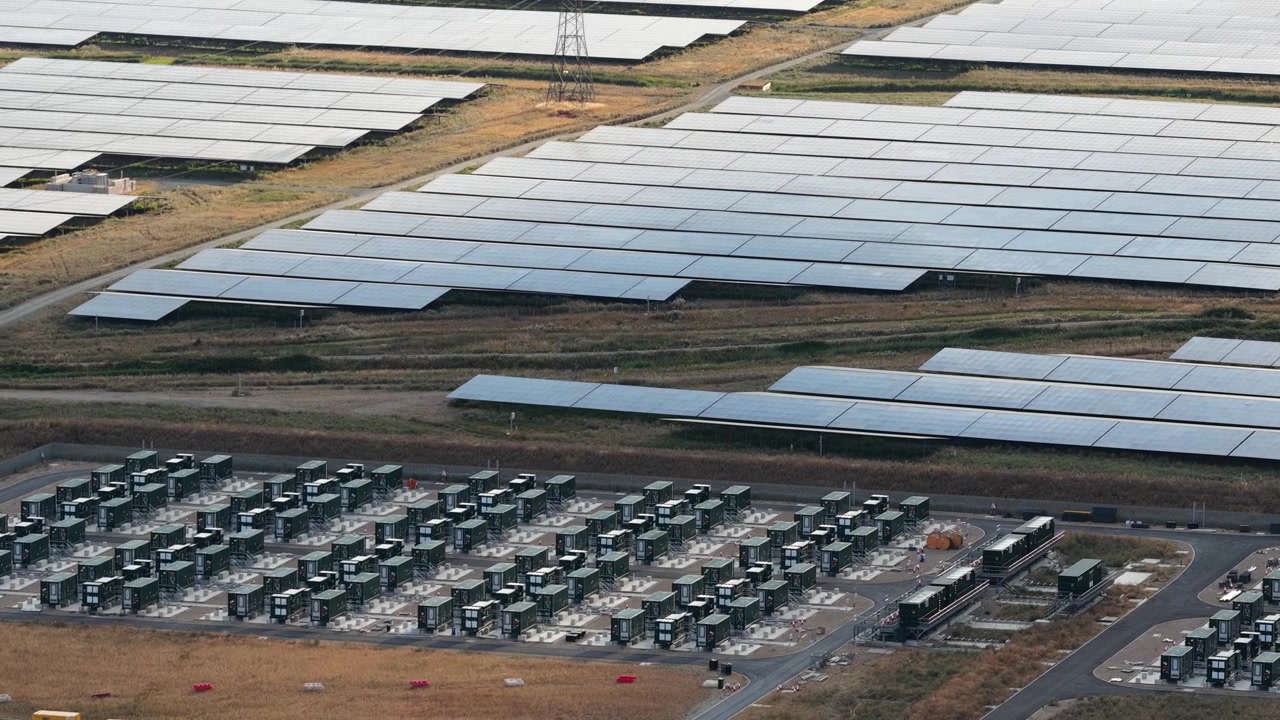 Perspektywa lotnicza prezentująca wielkoskalową elektrownię słoneczną z rzędami paneli fotowoltaicznych i przyległym systemem magazynowania energii akumulatorowej do przechowywania odnawialnej energii elektrycznej.