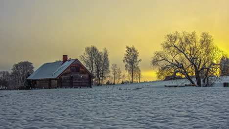 Time-lapse-shot-of-mystic-golden-sunset-behind-dense-clouds-during-snowy-winter-day-in-rural-area-with-farm-house