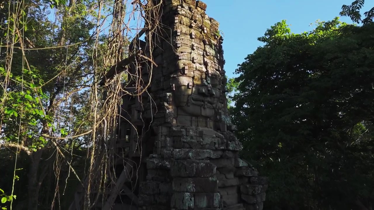 Volti di Buddha in arenaria su strutture templari in un complesso nella giungla remota vicino al confine thailandese. Volo aereo con drone attraverso la giungla con liane e radici