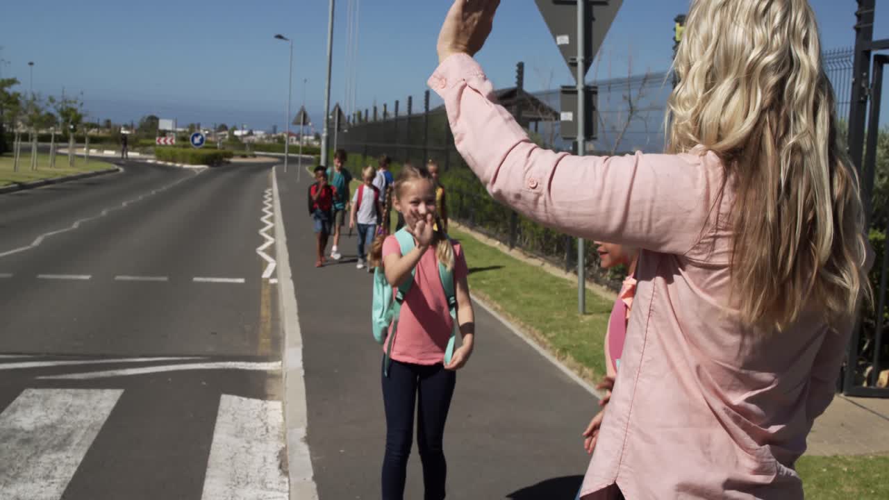 maestra agitando a dos niñas mientras cruzan la carretera