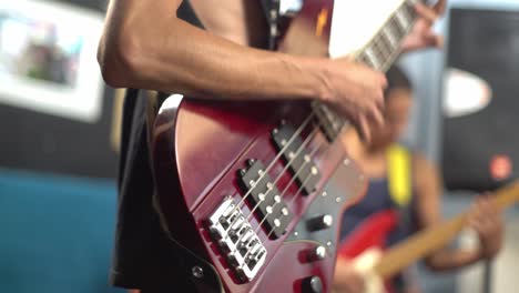 close-up of hand playing red electric bass, guitarist in background