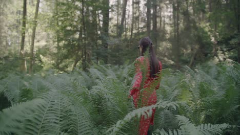 paseo por el bosque encantado: una mujer con un vestido rojo vibrante caminando a través de un bosque vibrante y de cuento de hadas entre helechos gruesos y exuberantes