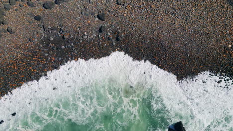 vista aérea hermosas olas rodando en la orilla del mar con piedras oscuras. océano espumando