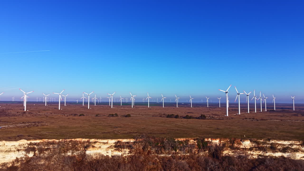 Turbinas eólicas enfileiradas em uma vasta paisagem sob um céu azul claro em uma área remota durante o dia.