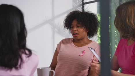 group of women wearing pink breast cancer awareness ribbons meeting and talking at therapy support group for cancer treatment patients with counsellor