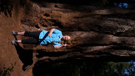 vertical shot of a hiker doing a dance trend in front of a large tree