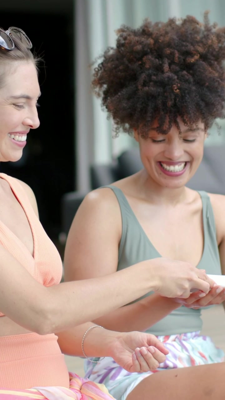 Vertical video: Passing women in swimwear applying lotion from white bottle on deck, sun urging