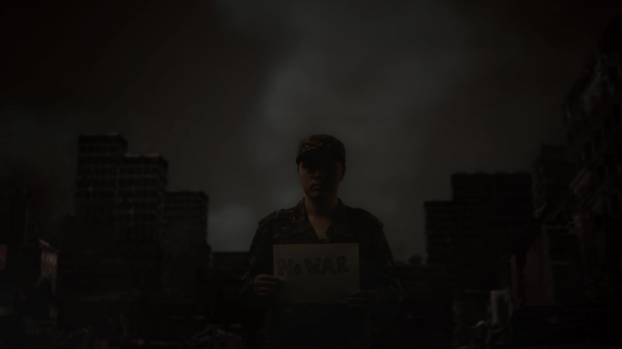 Asian Male Soldier Looking At Camera, Holding A Paper With Slogan No War While Standing In The Midst Of A Ruined City After A War