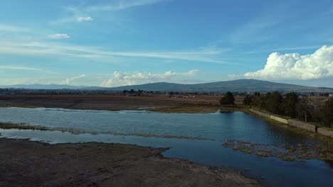 Aerial-orbit-over-a-small-wetland-with-mountains-and-cumulus-clouds-in-the-background