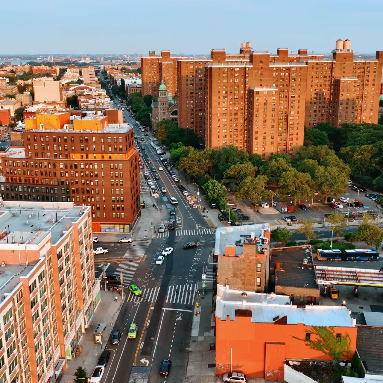 Setting sun lighting the orange blocks of flats in New York. Drone flies above the wide highways with numerous cars on