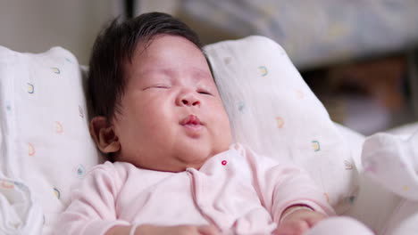 stretching and smiling a little, a tiny newborn baby is sticking out her tongue as she slowly dozes off to sleep