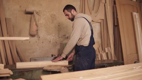 the carpenter cuts off the sides of the wood block on the circular saw. wooden shavings. the workshop is filled with wooden products