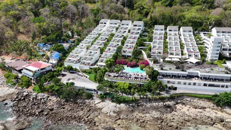 drone footage captures a scenic beachfront resort in phuket, thailand, showcasing lush greenery, clear waters, and vibrant architecture